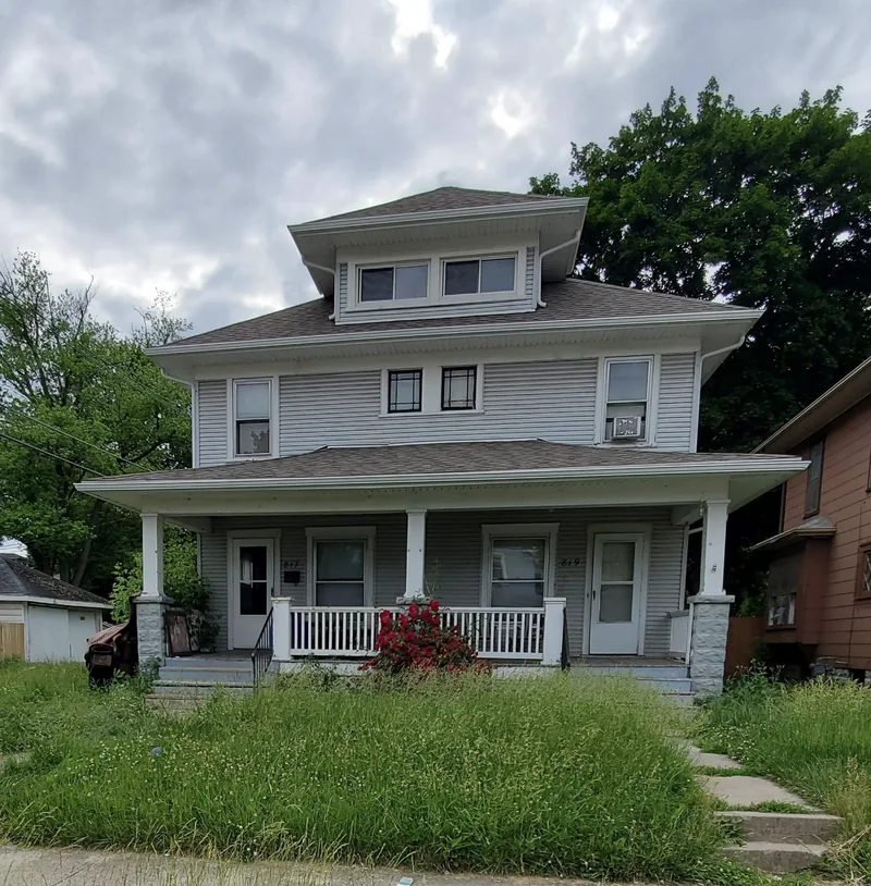 Springfield, OH rental duplex before EZ Rent Now rehab &mdash; overgrown lawn, unpainted porch and dated exterior